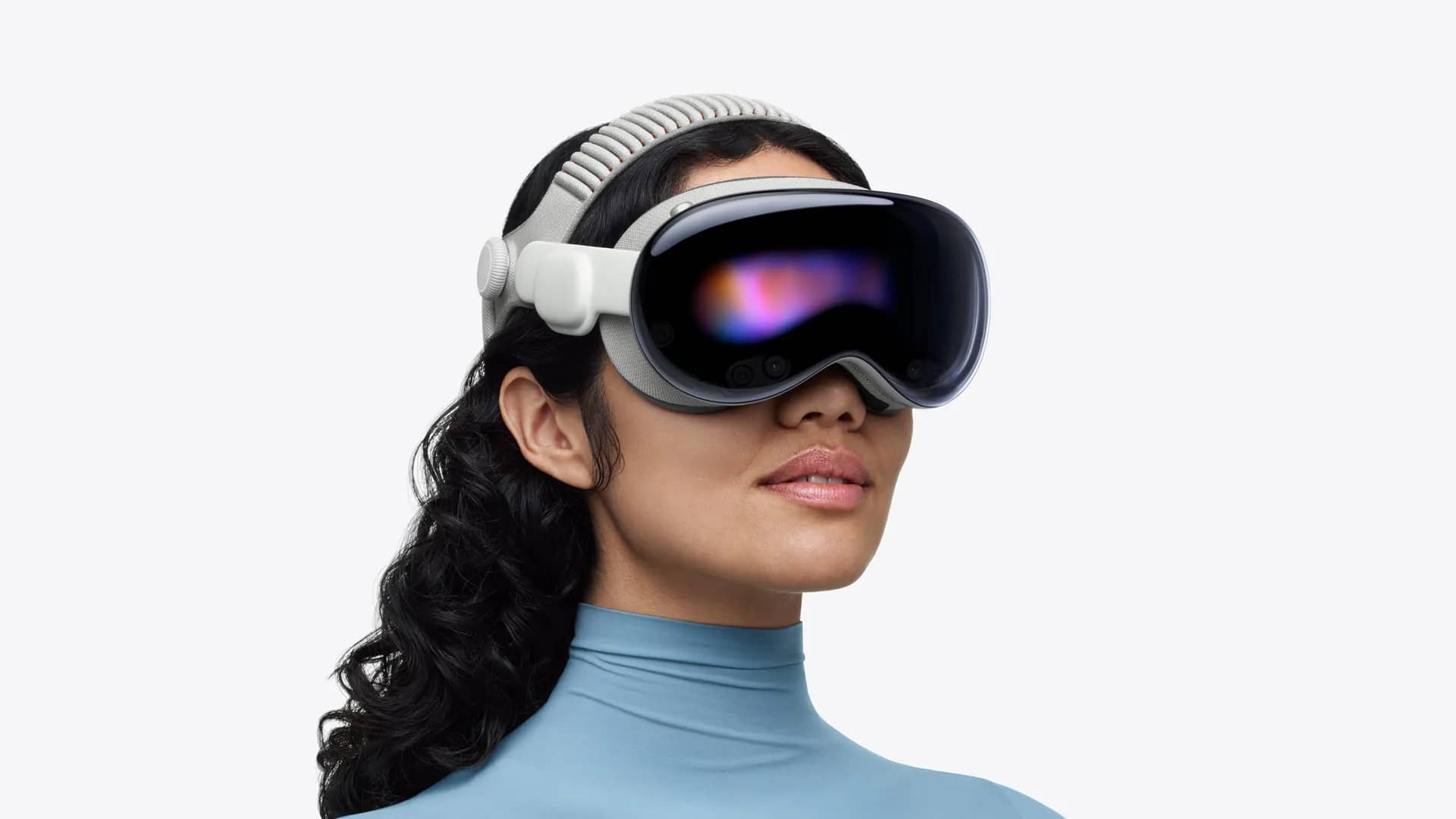 Woman wearing a silver Apple Vision Pro headset against a white background, screens glowing under the visor