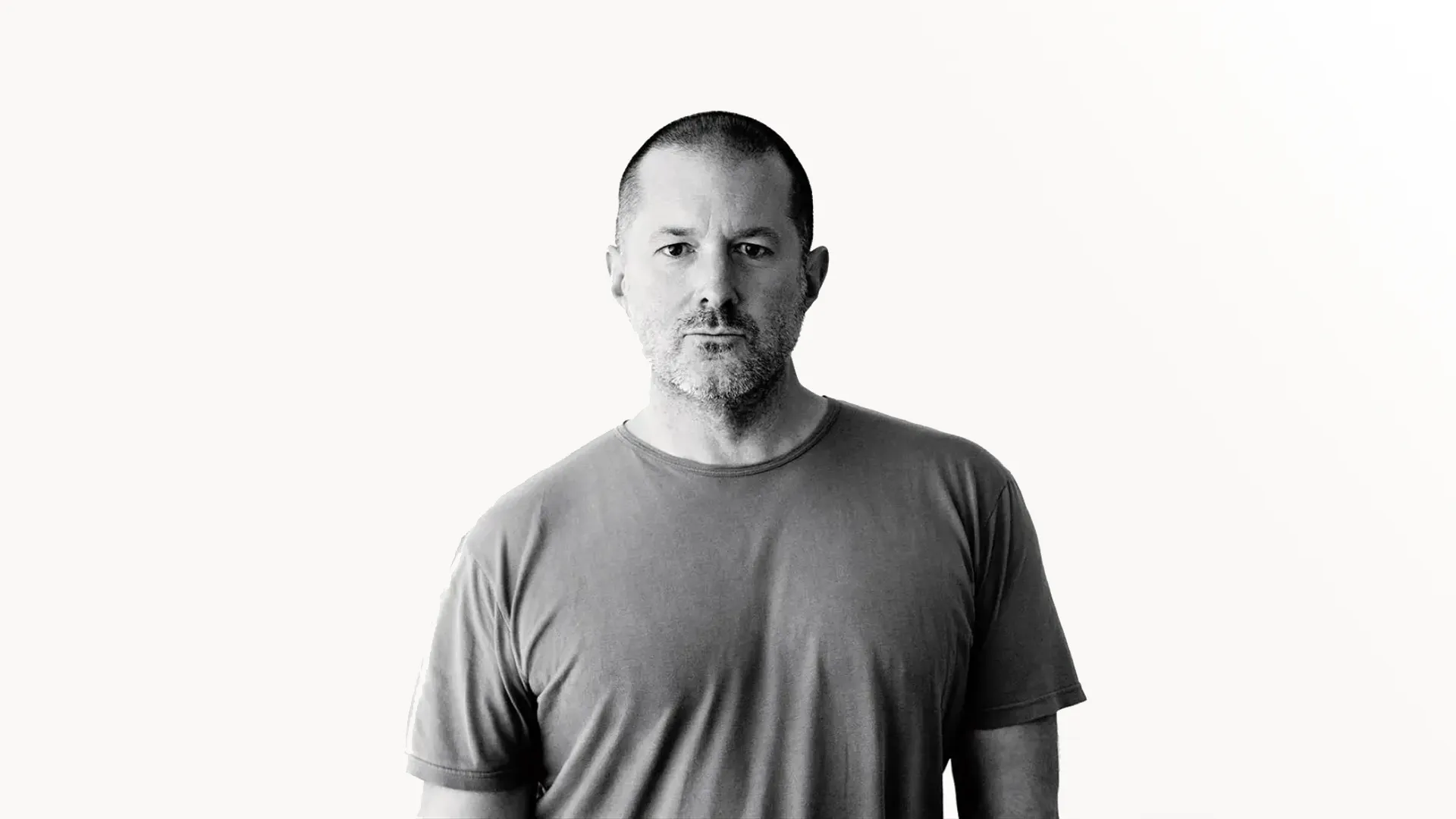 Minimalist black-and-white portrait of a designer in a plain gray t-shirt against a clean white background, evoking executive design leadership and restraint
